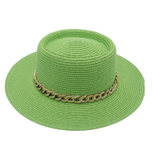 Detail of green straw boater hat featuring a thick gold metal chain decorative band