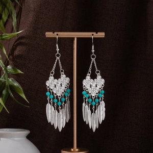 Detail of Bohemian silver feather earrings with blue beads on a metal display stand