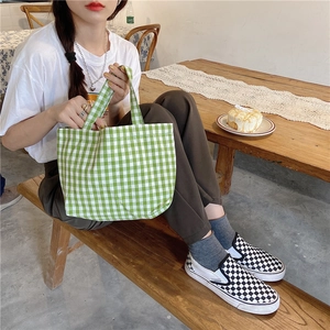 Detail shot of a green checkered cotton tote bag held by a model in a cozy cafe setting