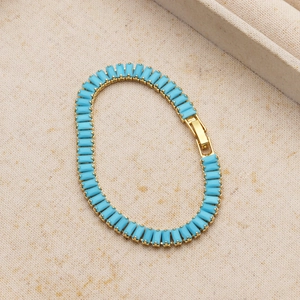 Detail of 18K gold-plated bracelet featuring turquoise-colored stones on beige linen