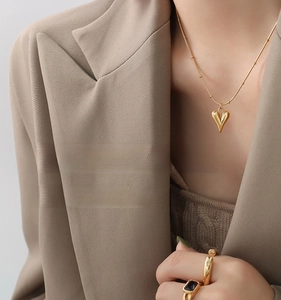 Detail shot of a gold heart pendant necklace and rings on a model in a beige suit
