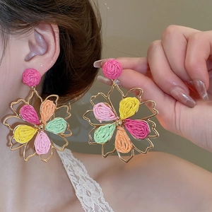 Detail view of colorful woven floral earrings with golden metal frames and vibrant texture