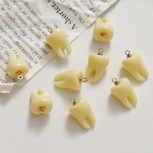 Detailed view of 3D resin tooth-shaped charms with golden metal loops on white background