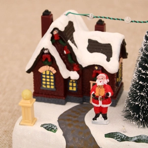 Close-up of a Christmas resin music box with miniature Santa, snowy house, and LED lights
