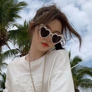 Outdoor shot of heart-shaped sunglasses with white frames and dark lenses on a model