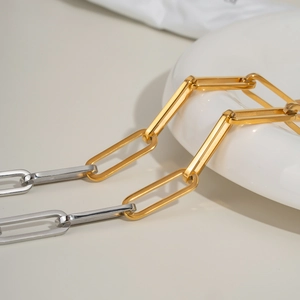 Detail of two-tone gold and silver rectangular link chain necklace on a white ceramic plate