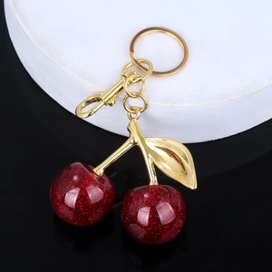 Macro shot of glittery cherry keychain with gold leaves on a black reflective base