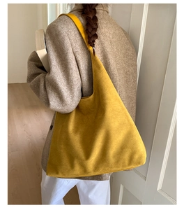 Detail of a large yellow faux suede tote bag with a wide shoulder strap worn by a model