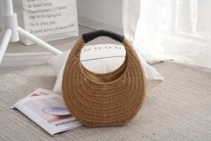 Detail of hand-woven straw handbag featuring black leather handles and crescent shape