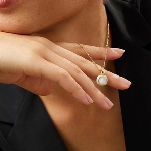 Close-up of 18k gold plated necklace with white shell pendant on a model in a black suit