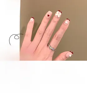 Detail of pink press-on nails with red French tips, 3D white bows, and heart patterns
