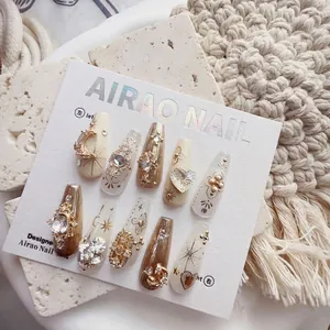 Detail of luxury press-on nails with ivory base, gold 3D charms, and sparkling rhinestones