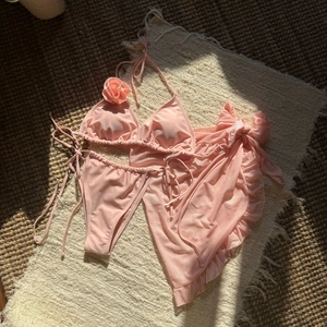 Detailed flat lay of pink three-piece bikini set with mesh skirt and 3D floral accents