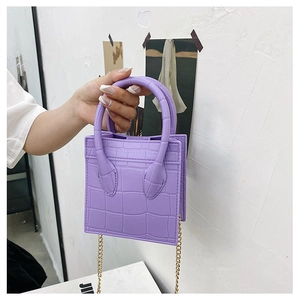 Detail of purple crocodile pattern mini bag with golden chain strap on a white wall