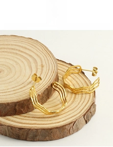 Detail showing 18k gold plated stainless steel wave earrings on a wooden texture base