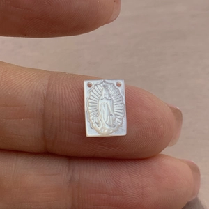 Macro shot of hand holding a carved white mother of pearl Guadalupe shell pendant