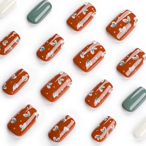 Orange press-on nails with white heart patterns and complementary green and white solid tones