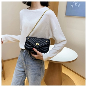 Close-up of black quilted leather crossbody bag with golden chain strap on shoulder