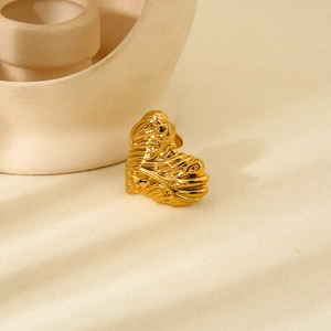 Close-up of golden textured heart ring on neutral fabric background with soft shadows