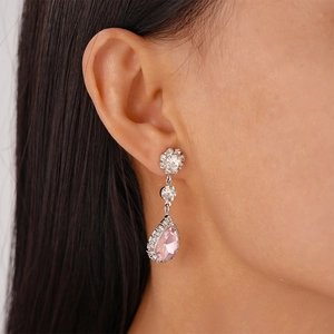 Close-up of pink teardrop earrings with halo diamonds on a female model's ear