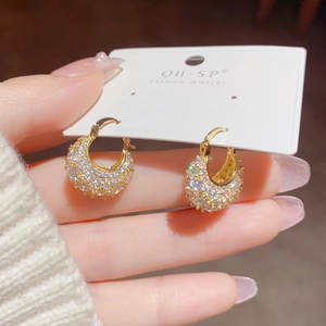 Detailed close-up of golden C-shaped hoop earrings paved with sparkling cubic zirconia