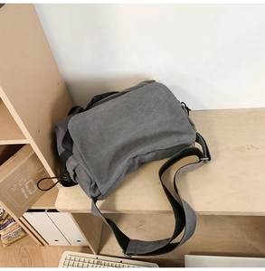 Close-up of grey canvas messenger bag with adjustable strap on a wooden shelf
