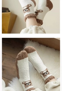 Close-up of cozy coral fleece bear socks with brown trim on white plush carpet