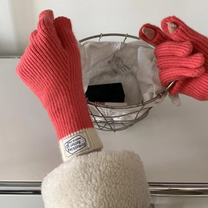 Detail of pink knitted touchscreen gloves with beige cuffs and a sewn-on label design