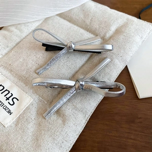 Detail view of two silver Y2K faux leather bow hair clips on a textured canvas bag