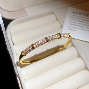 Macro shot of gold plated zircon pavé bangle resting on a cream velvet jewelry box