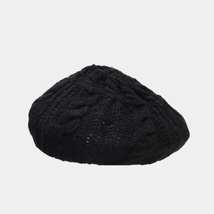 Close-up of black cable knit beret showing textured wool pattern on gray background