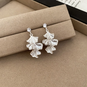 Detailed view of silver ginkgo leaf earrings with sparkling zircon stones on a beige stand