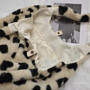 Close-up of the plush cow print tote bag showing white satin lining and metal snap button