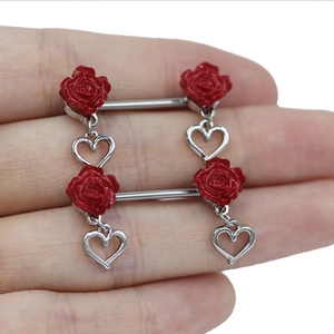 Close-up of heart-shaped pendants and red rose charms on stainless steel nipple rings