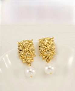 Close-up of gold woven texture earrings with elegant white pearl drops on a white plate