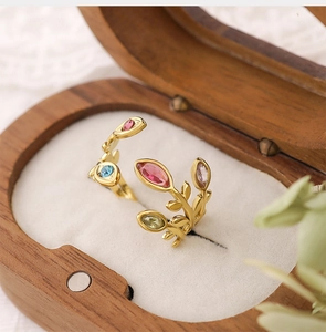 Macro detail of 18K gold leaf ring with colorful zircons on a wooden jewelry box
