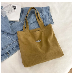 Flat lay of khaki canvas tote bag on white sheets with denim jacket and fashion book