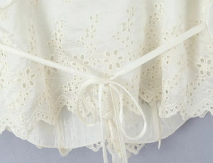 Detailed close-up of white ruffled camisole with delicate embroidery and bow tie detail