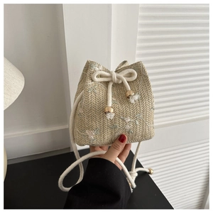 Detail of woven straw bucket bag featuring floral embroidery and white tassel drawstring