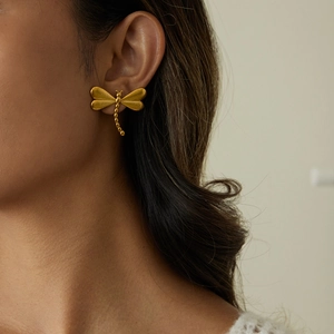 Gros plan sur un clou d'oreille libellule or mat avec chaîne perlée porté par un mannequin