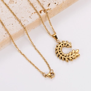 Golden necklace with leaf-shaped crescent pendant displayed on minimalist stone