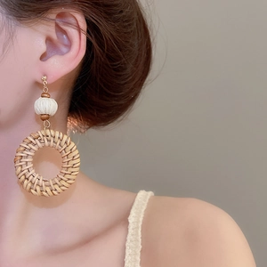 Detail of bohemian hand-woven rattan hoop earring with wooden beads worn by a model
