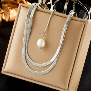 Close-up of layered silver necklace with flat snake chain and white pearl eye pendant