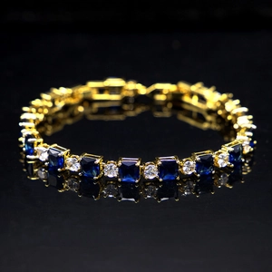 Detail of gold bracelet with alternating blue square and clear round zircons on black surface