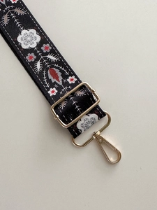 Detail of black canvas strap with multicolor floral embroidery and golden metal hooks
