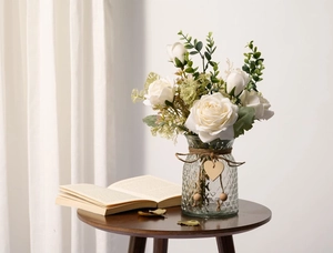 Artificial white roses in a diamond texture glass vase on a wooden table with book