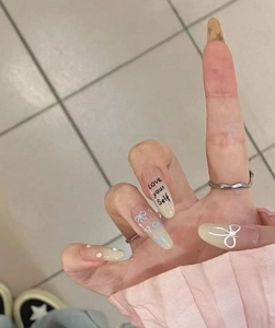 Detail of gradient press-on nails with white bows, pearls, and Love Yourself lettering