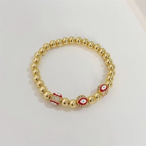 Macro shot of 18K gold beaded bracelet with red enamel evil eye and micro-inlaid crystals