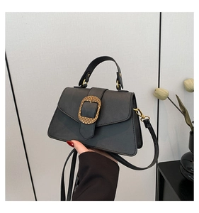 Detail of black crossbody bag with large gold woven textured buckle and leather handle