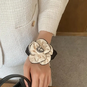 Elegant camellia flower scrunchie in cream with black borders worn on a wrist